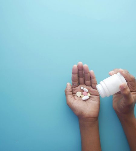 Politique d'expédition Hands pouring pills from a bottle on a blue background, representing healthcare and medication.